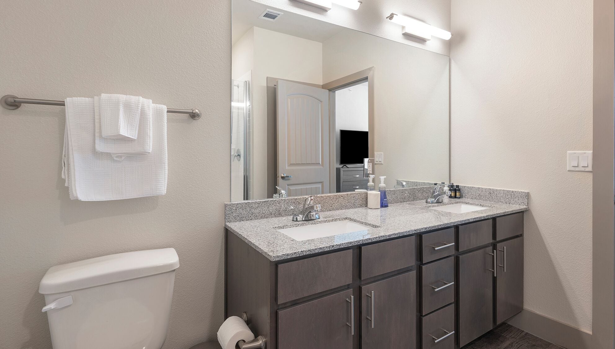 Un baño moderno con tocador de doble lavabo, inodoro y espejo grande.