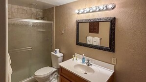 Et badeværelse med bruser, toilet, vaskebord med spejl og et oplyst område ved vaskebordet.