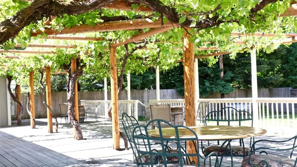 Eine überdachte Terrasse mit Tisch und Stühlen, umgeben von hölzernen Pergolas und einem Holzboden.