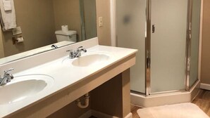 Ein Badezimmer mit großem Spiegel, zwei Waschbecken, einer Duschkabine und einer Toilette.