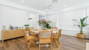 A dining area with a round table, six chairs, a ceiling fan, and a window with blinds.