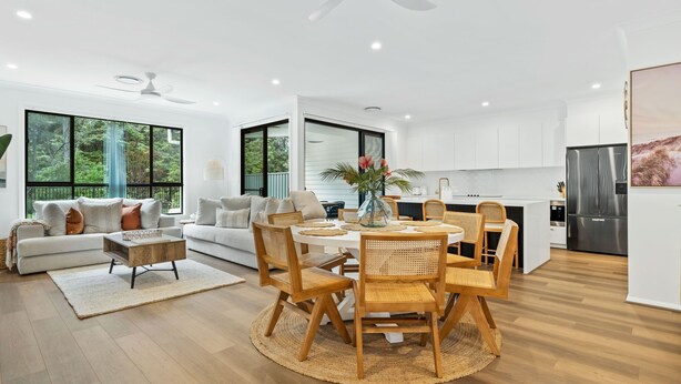 A modern kitchen with a built-in refrigerator, dining table with chairs, and a large window overlooking greenery.