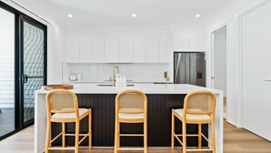 A modern kitchen with white cabinets, a stainless steel refrigerator, and three wooden chairs.