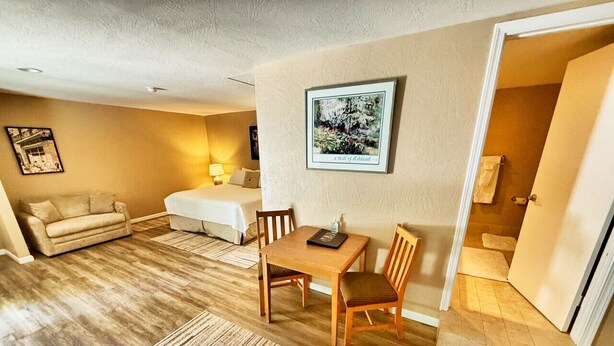 A living room with a wooden floor, a sofa, a dining table with chairs, and a framed picture on the wall.