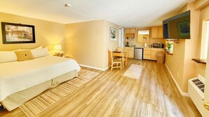 A compact hotel room with a bed, bedside table, and a small kitchenette.