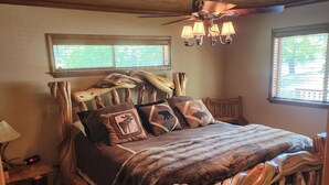 A rustic wooden bed with a unique design, a ceiling fan, and two windows with blinds. - Augustino Vineyard Winery Cabin Cave Junction (O'Brien)