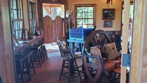 A rustic interior with wooden floors, a dining area with chairs and a table, a large decorative chair, and a chandelier. - Augustino Vineyard Winery Cabin Cave Junction (O'Brien)