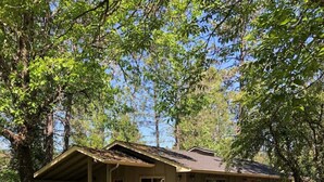 A two-story cabin with a porch, surrounded by trees and grass. - Augustino Vineyard Winery Cabin Cave Junction (O'Brien)