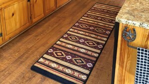 Une cuisine avec des meubles en bois, un plan de travail en granit, un réfrigérateur noir et un tapis à motifs.