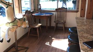 Una habitación con piso de madera, una mesa redonda con sillas, una barra y un ventanal con vistas a árboles y un coche afuera.