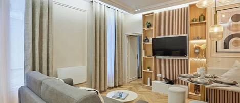 A modern living room with a sofa, ottoman, TV, and a dining area with a table set for two.