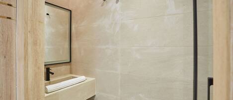 A modern bathroom with a wooden vanity, a mirror, and a shower area.