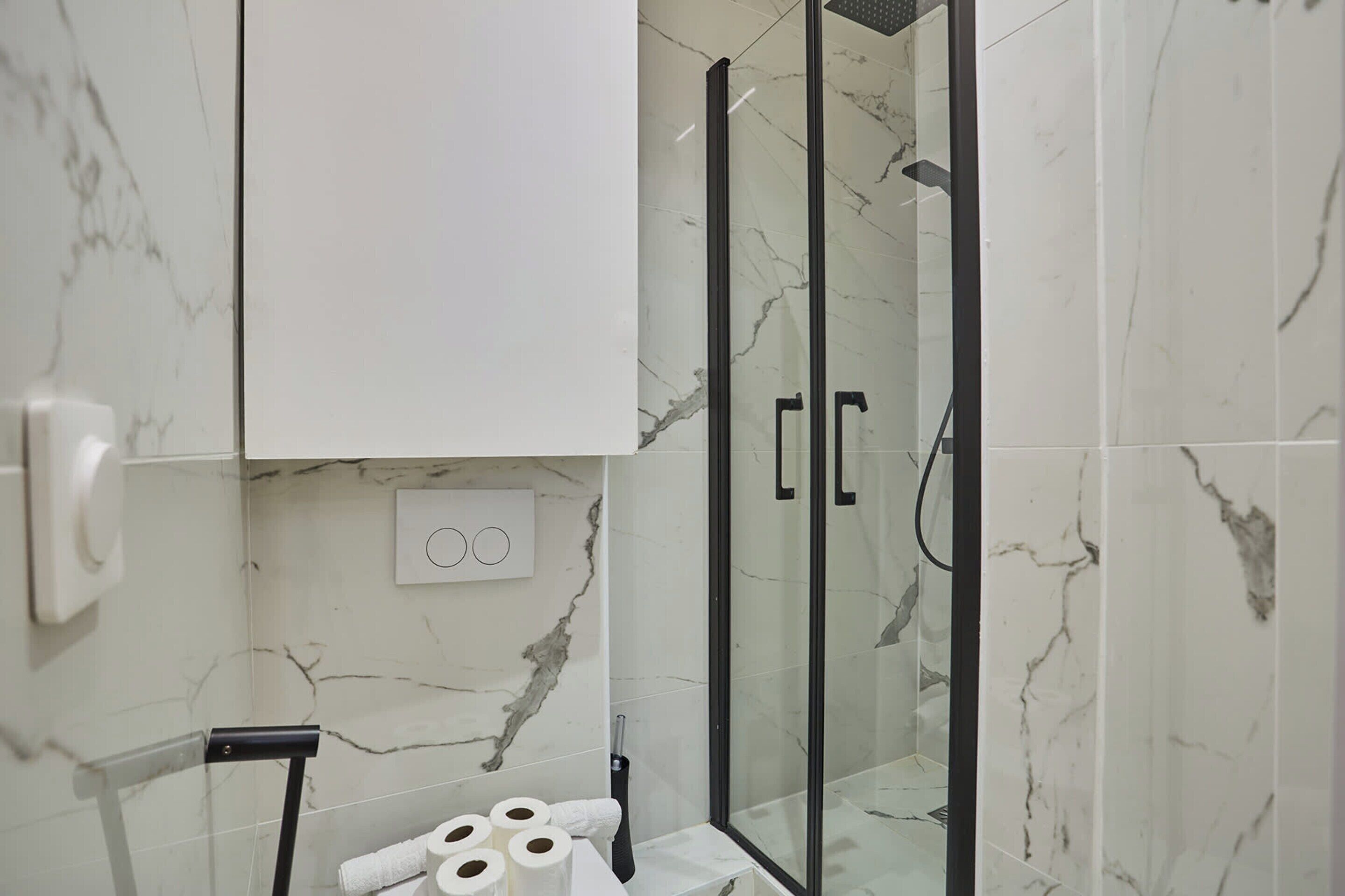 Une salle de bain avec une douche à parois de verre, des murs en marbre et un meuble blanc.