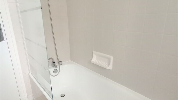 Un baño moderno con mampara de vidrio, bañera blanca y pared con azulejos color beige.
