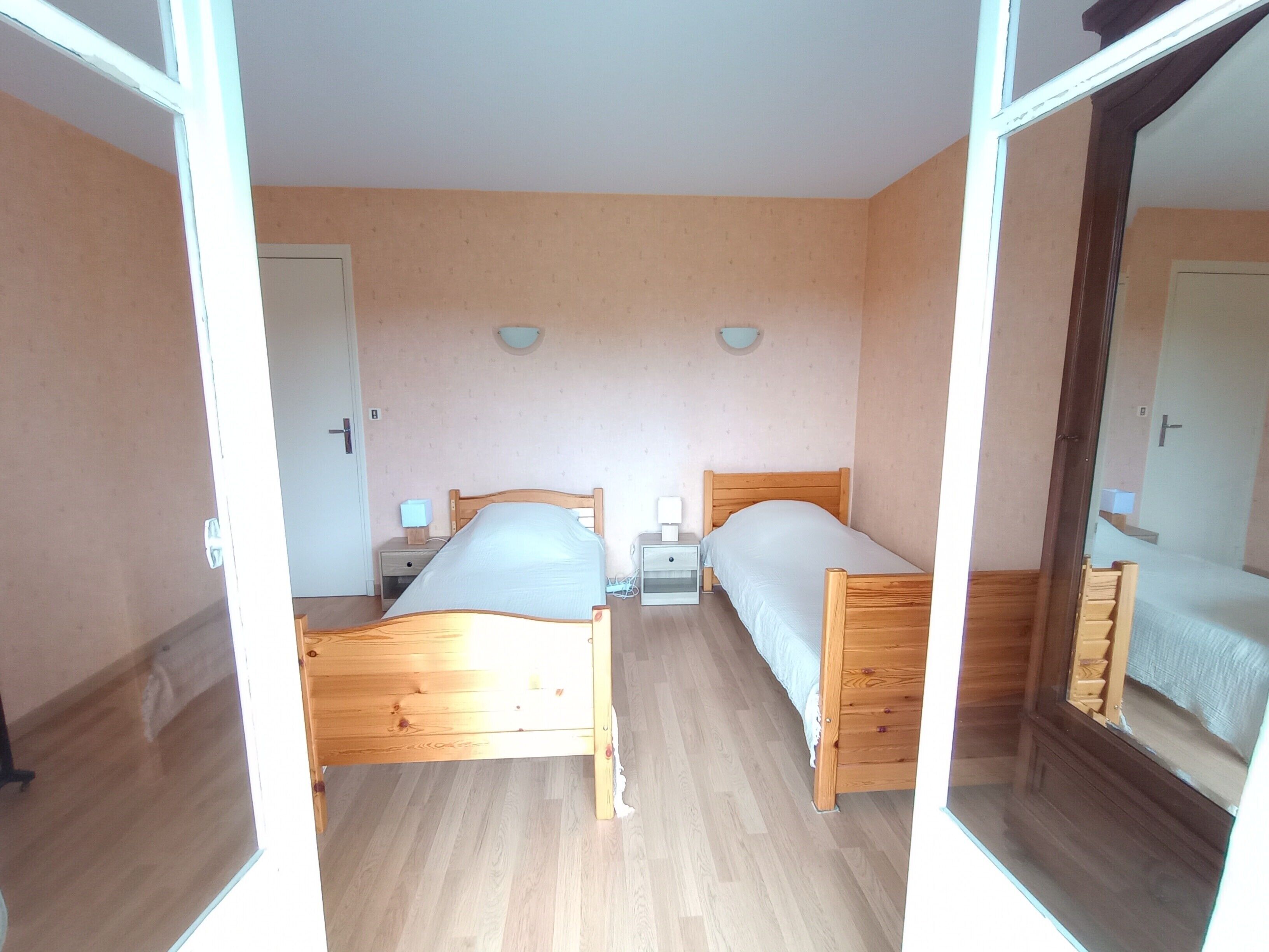 Une pièce avec deux lits en bois, une petite table de chevet avec une lampe, un luminaire fixé au mur et une porte.