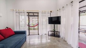 A living room with a blue sofa, a flat-screen TV, and a glass door leading to an outdoor area. - Villa Milu, Pool, Avellanas (Tamarindo)