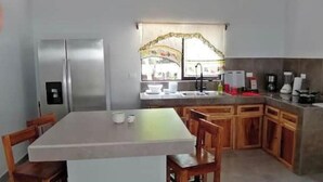 A compact kitchen with a refrigerator, a sink, and a dining area with chairs. - Villa Milu, Pool, Avellanas (Tamarindo)