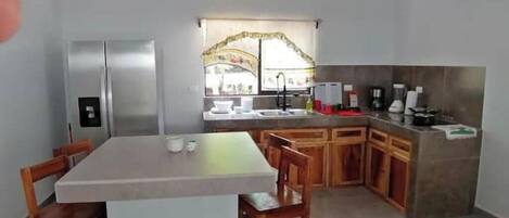 Una cocina compacta con refrigerador, lavamanos y comedor con sillas.