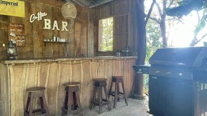 A rustic bar with wooden walls and a sign that reads "Coffee BAR". There are three stools and a grill to the right.