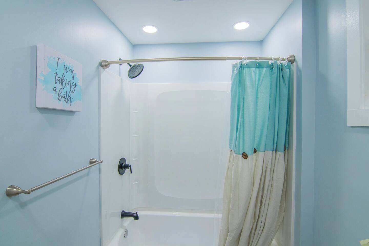 A bathroom with a shower, a handrail, a towel rack, and a motivational quote on the wall.