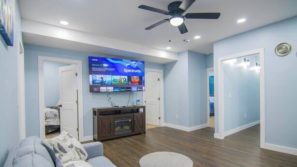 Un salon moderne doté d’un téléviseur à écran plat fixé au mur, d’un ventilateur de plafond et d’un meuble de rangement en bois pour les appareils multimédias.