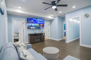 A modern living room with a flat-screen TV mounted on the wall, a ceiling fan, and a wooden entertainment center. - Cozy 2nd & 3rd Floor Retreat (Lewiston)