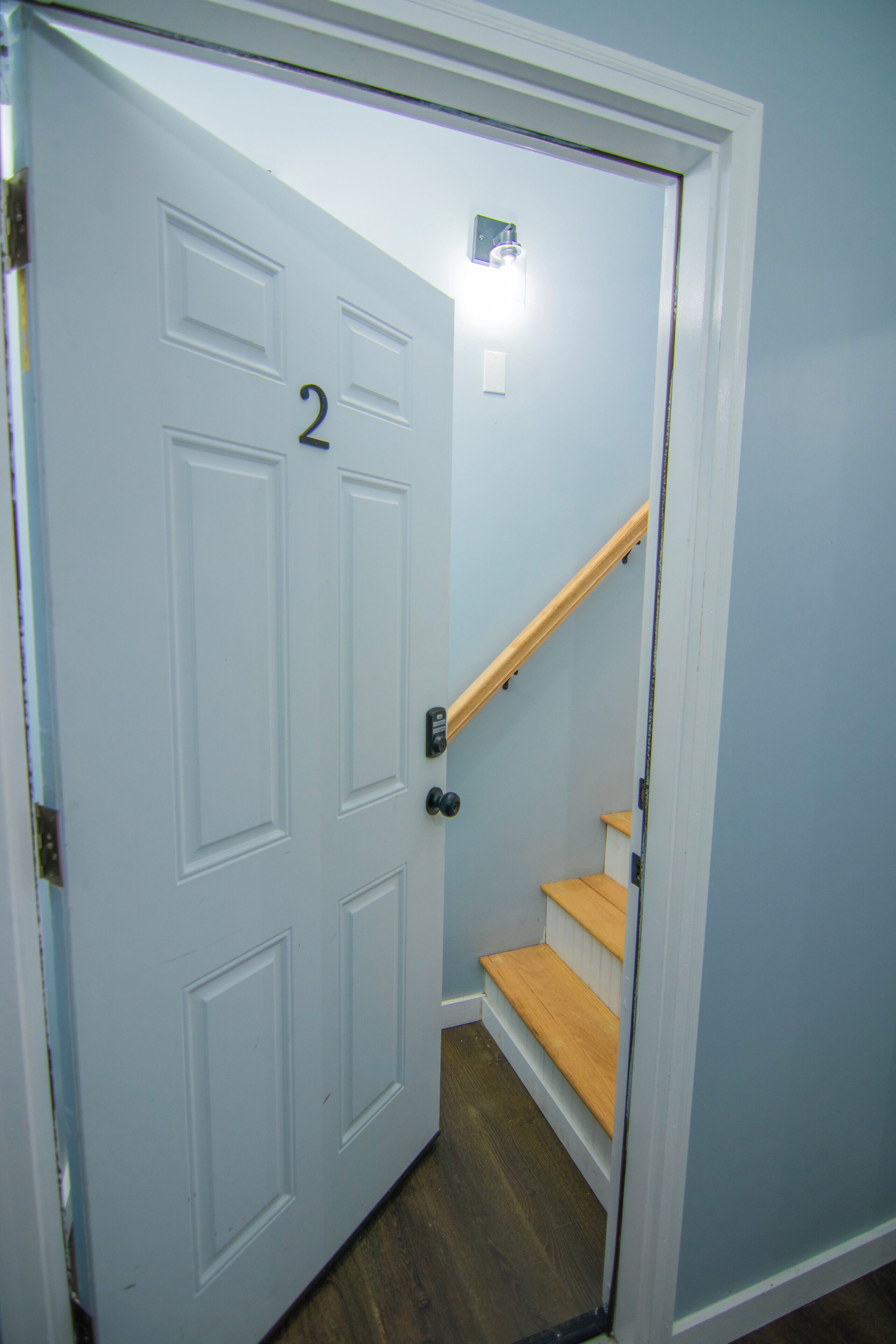 A white door with the number 2, a wooden staircase, and a light fixture above the door.