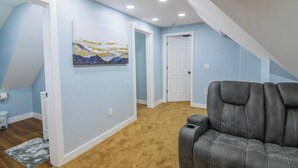 Une pièce avec un plafond haut, des spots encastrés, un tableau au mur, une porte et un fauteuil en cuir.