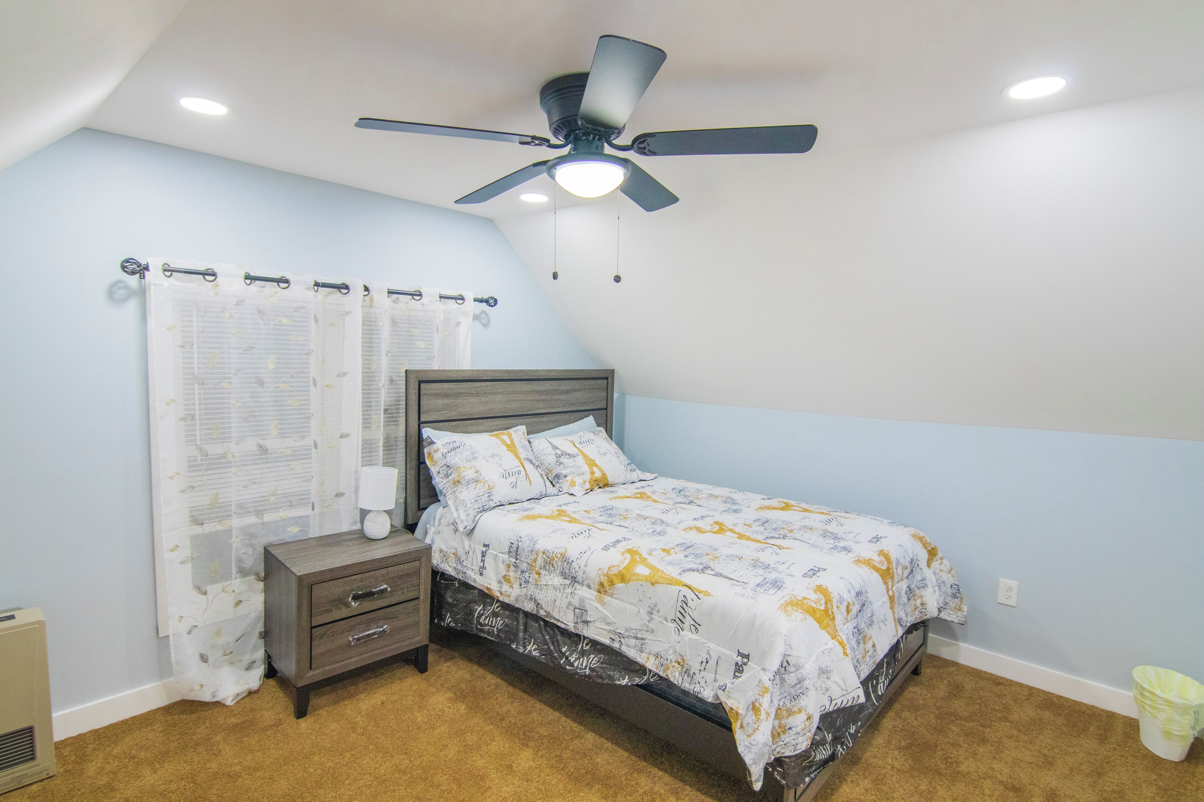 Un dormitorio con cama, mesita de noche y ventilador de techo.