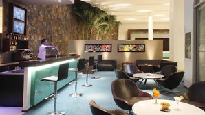 A bar area with a bartender, bar stools, and a counter with bottles. There are several tables and chairs in the seating area. - Apartment Hotel estelar (Barranquilla)