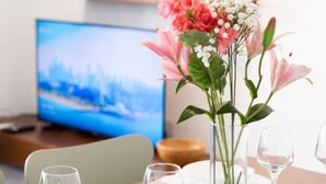 Una mesa de comedor dispuesta con platos blancos, copas y un florero con flores rosa y blancas.