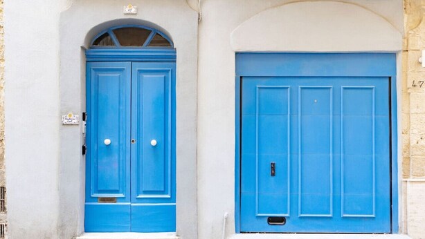 Una puerta azul con un pequeño ventanal arriba y una puerta más grande con un picaporte.