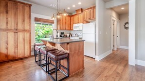 A modern kitchen with wooden cabinets, a central island with stools, and a view of greenery outside.