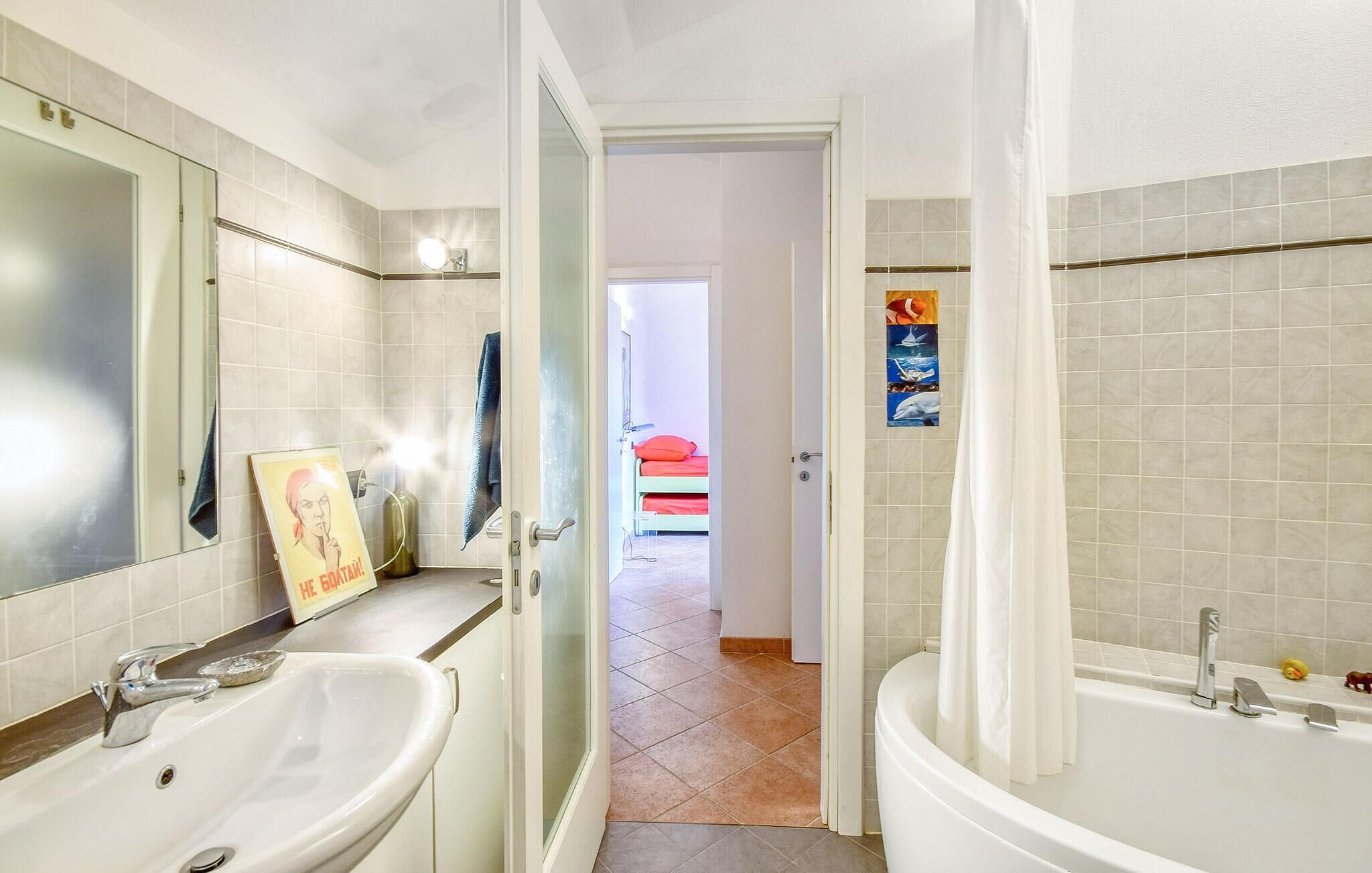 A bathroom with a sink, mirror, and bathtub. There is a door leading to a bedroom with a bed and a poster on the wall.