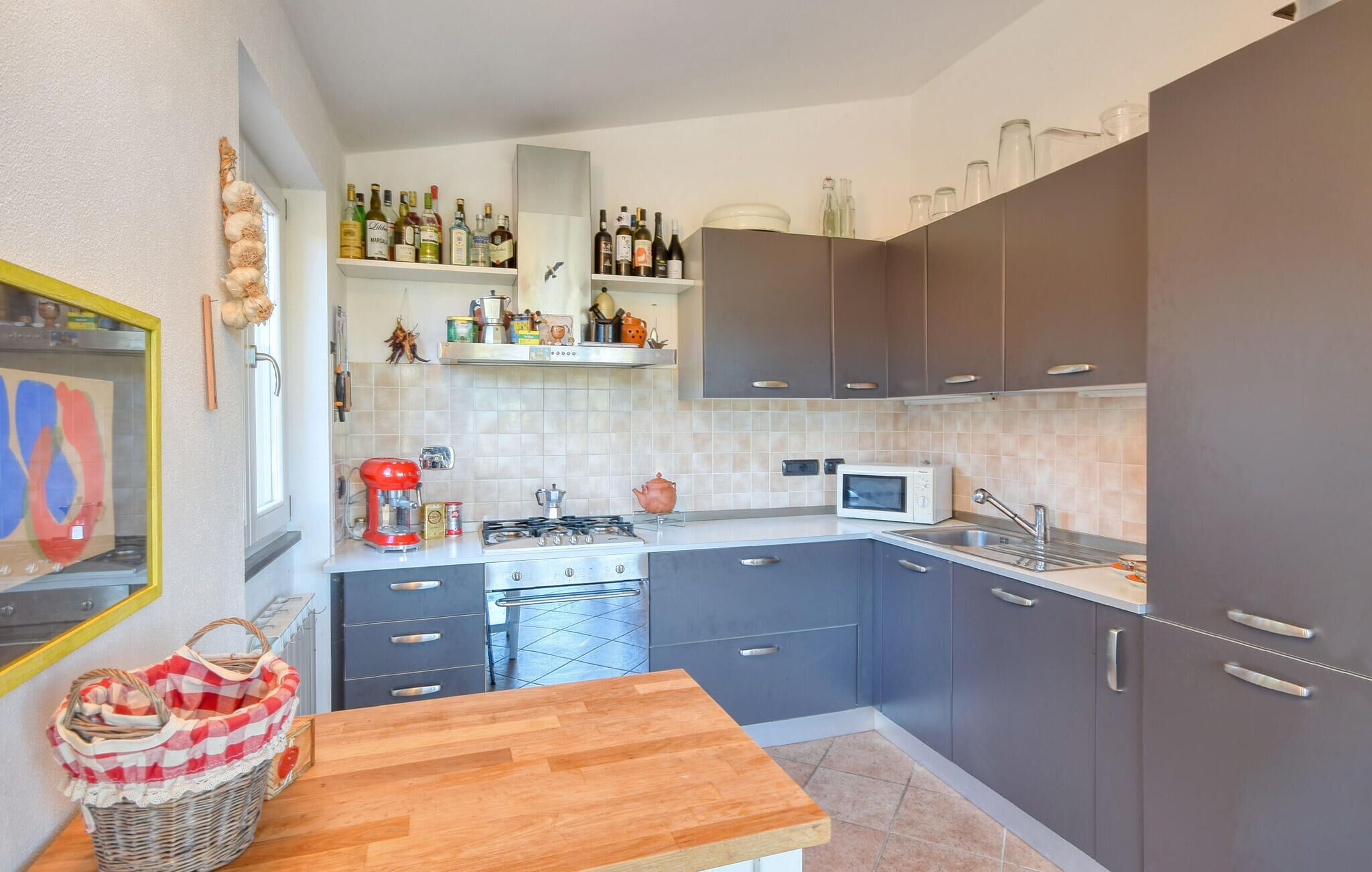 Una cocina compacta con estufa a gas, microondas y diferentes electrodomésticos. Hay armarios, una encimera y una pequeña zona de comedor con una mesa de madera.