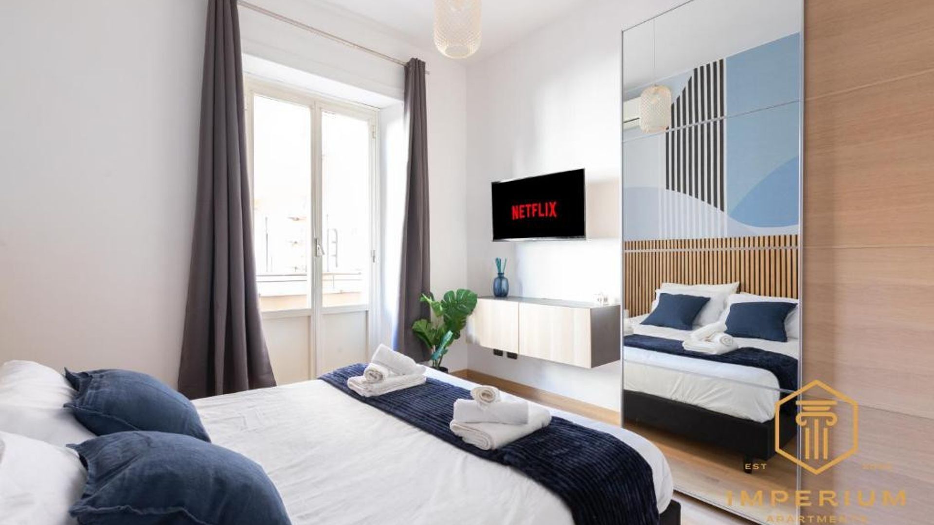 A hotel room with a bed, a TV displaying Netflix, a mirror, and a view of a balcony.