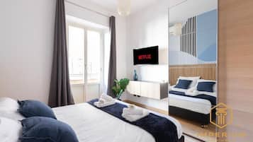 Una camera d'albergo con un letto, una TV che mostra Netflix, uno specchio e vista su un balcone.