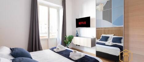 Quarto de hotel com cama, televisão exibindo Netflix, espelho e vista para uma varanda.