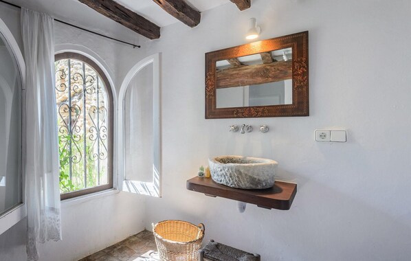 Relax in this serene bathroom with an arched window, wooden beam ceiling, and stone basin sink.