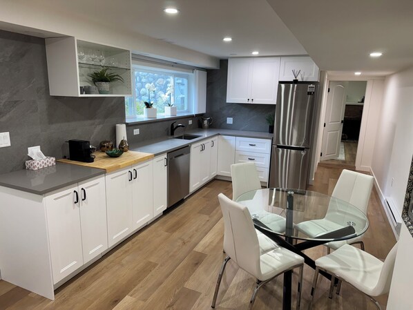 Una cocina moderna con armarios blancos, un refrigerador de acero inoxidable y un comedor con mesa de vidrio y sillas blancas.