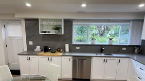 Een moderne keuken met witte kasten, een roestvrijstalen vaatwasser, een houten aanrechtblad en een raam met uitzicht op groen.