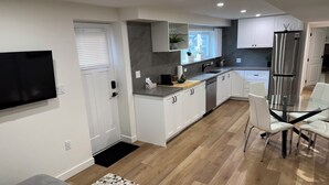 Een moderne keuken met witte kasten, een roestvrijstalen koelkast en een eethoek met een glazen tafel en witte stoelen.