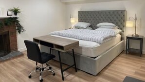 Een slaapkamer met een bed, een bureau, een stoel, een open haard en twee bedlampen.