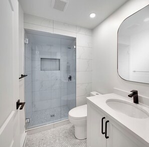 Un baño moderno con ducha de mampara de vidrio, inodoro blanco y tocador con espejo.