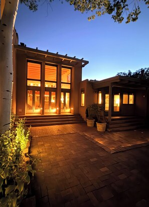A modern house with a large glass window, a brick pathway, and a tree.