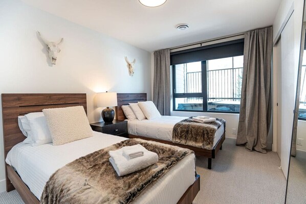 A hotel room with two beds, a large window with curtains, and a wall-mounted skull decoration.