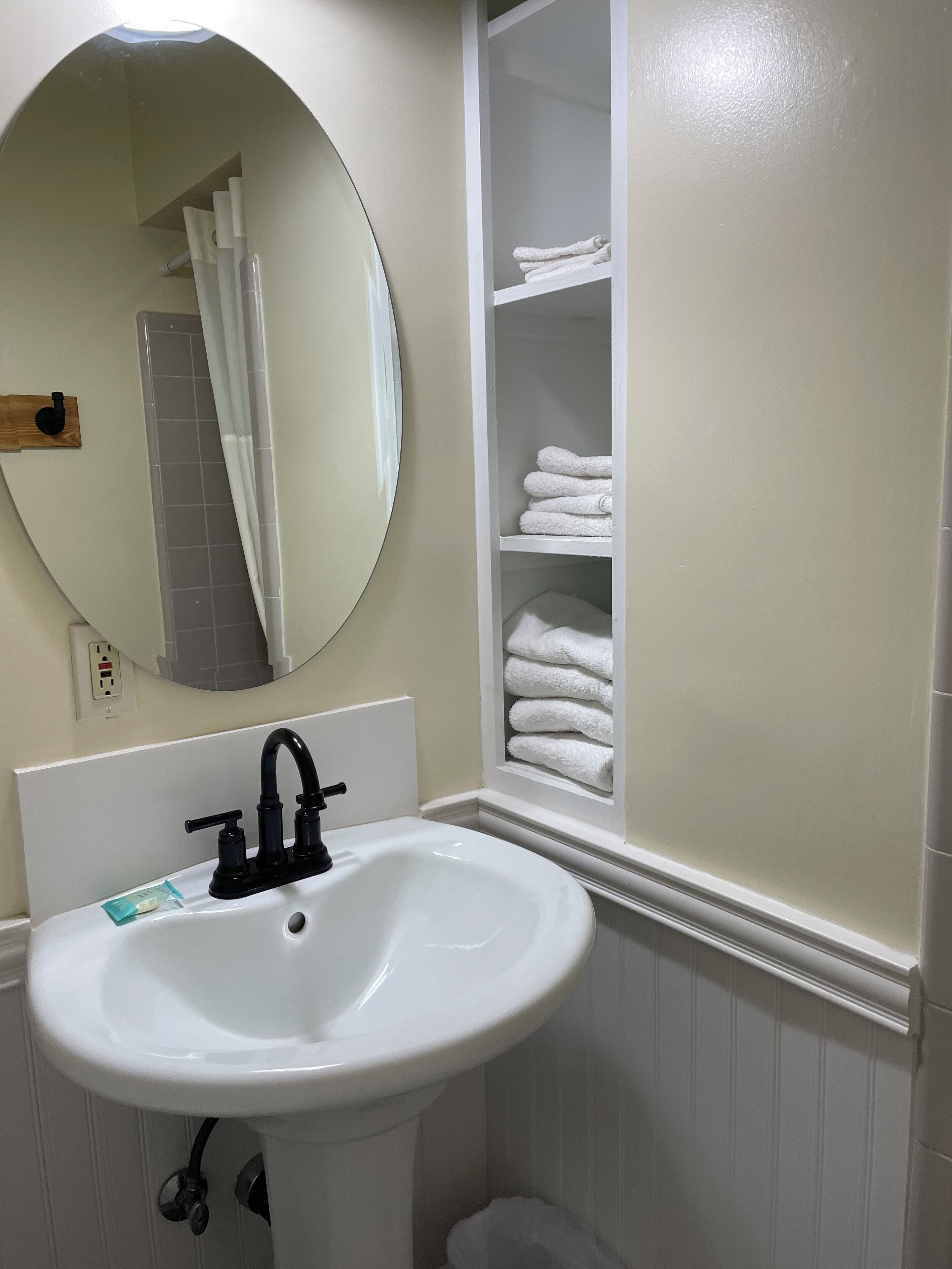 A bathroom with a white sink, a round mirror, and a towel rack.