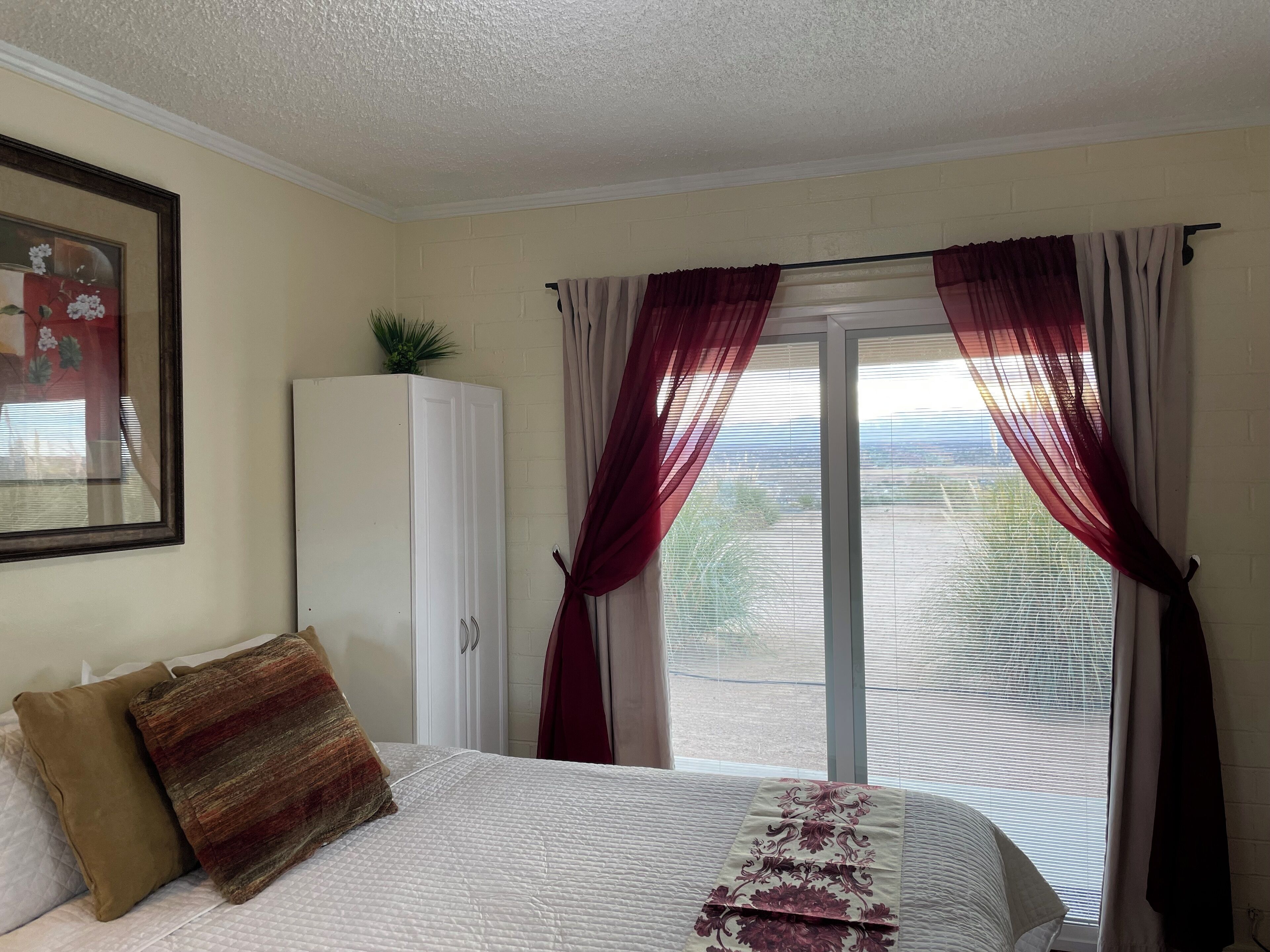 A bedroom with a bed, a wardrobe, a window with curtains, and a framed picture on the wall.