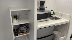 Una kitchenette pequeña equipada con microondas, cafetera y lavamanos.