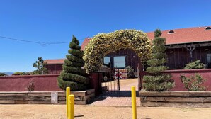 Un edificio con fachada de ladrillo rojo, un arco de madera cubierto de flores amarillas y un letrero que anuncia pollo, carne de res, cerdo y costillas.